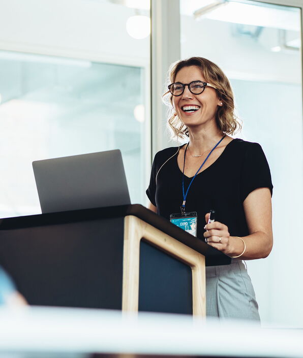 Frau steht mit Laptop am Podium und hält eine Rede