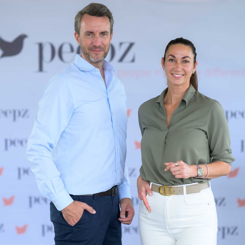 Geschäftsführung von peepz vor einer Branding-Wand mit Firmenlogo.