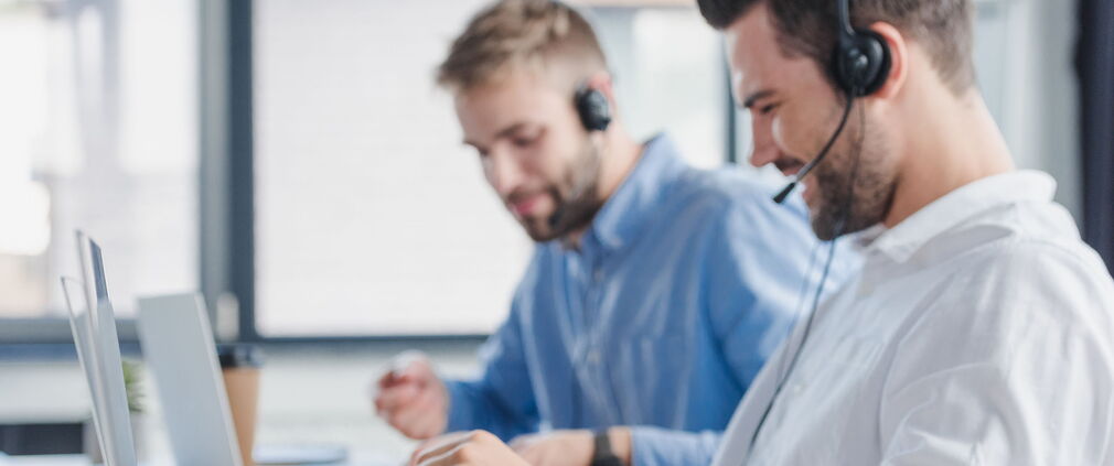Lächelnde Callcenter-Mitarbeiter mit Headsets und Laptops im Büro