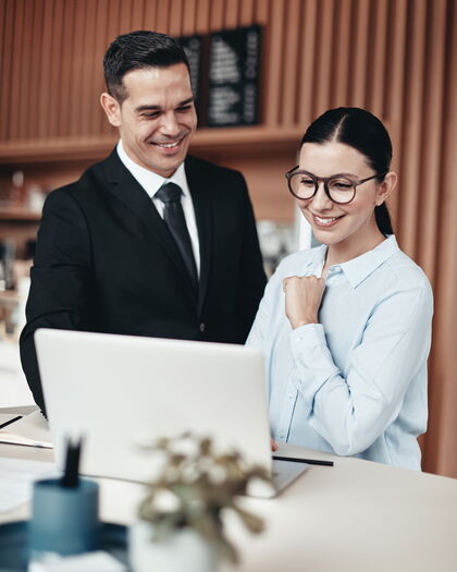 Zwei lächelnde Mitarbeiter am Empfang, die zusammen in einem Büro einen Laptop benutzen