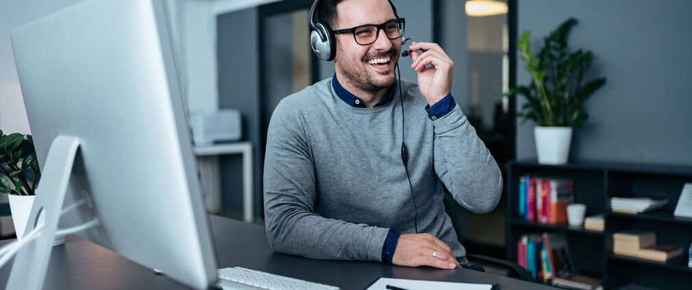 Zufriedener Mitarbeiter des technischen Supports mit Headset, der einen Kunden berät