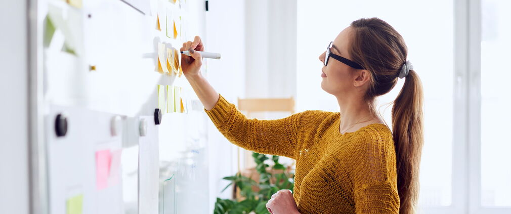 Mitarbeiterin plant mit Hilfe eines Whiteboards.
