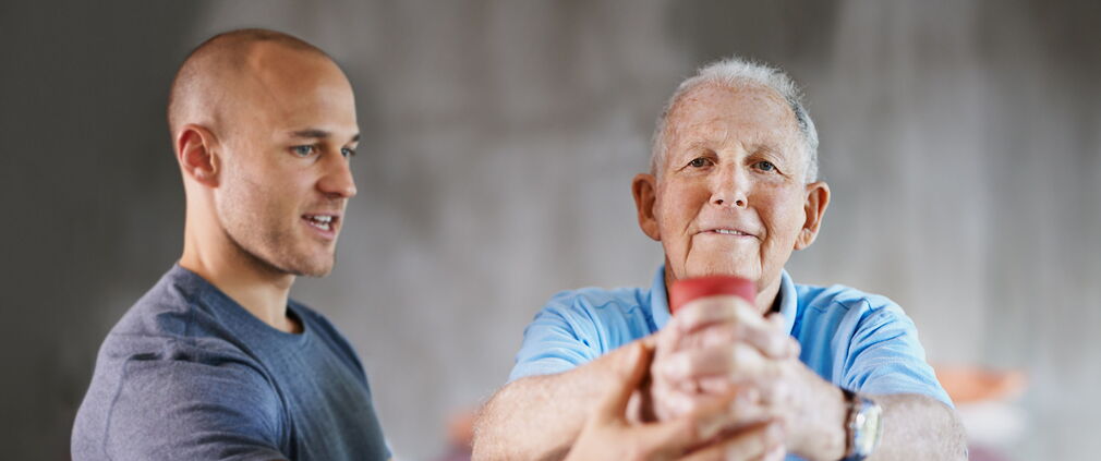 Aufnahme eines älteren Mannes, der mit Hilfe eines Physiotherapeuten trainiert