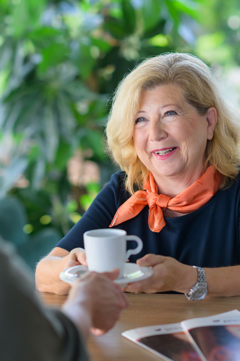 Empfangsmitarbeiterin reicht einer Besucherin im Beratungsgespräch eine Tasse Kaffee.