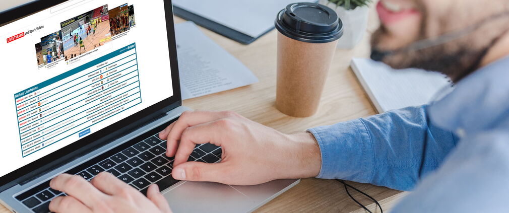 Aufnahme eines lächelnden Mitarbeiters, der auf seinem Laptop die Website www.sportdeutschland.tv besucht