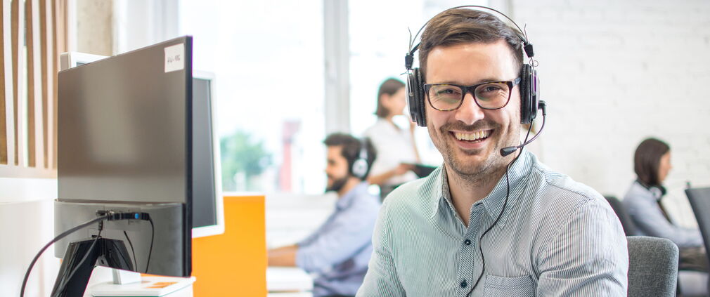 Männlicher Mitarbeiter im Telefonservice mit Headset bei der Arbeit