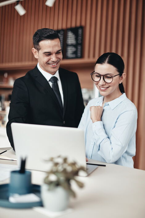 Zwei lächelnde Mitarbeiter am Empfang, die zusammen in einem Büro einen Laptop benutzen